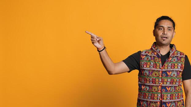 Salesman pointing around with finger, doing recommendation, talking with audience. Indian person showing copy text, doing advertisement, isolated over studio background, camera A photo