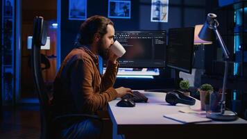 Focused programmer drinking coffee in apartment while solving database errors on computer. Remotely working IT admin concentrated on finalizing coding project in home office, camera B photo