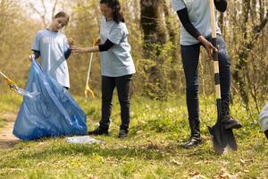 Group of environmentalists cleaning the forest from junk and plastic waste, grabbing trash with a long claw tool. Climate change activists picking up rubbish and recycling. photo