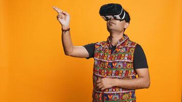 Indian man wearing virtual reality headset, doing swiping gestures. Technology enthusiast using high tech futuristic modern VR gadget, isolated over studio background, camera B photo
