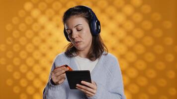 Woman reading ebook on ereader and listening music purchasing books online. Person with tablet looking to buy digital novel with credit card, hearing songs in headphones, studio background, camera B photo