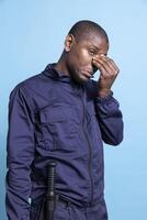 African american security guard deals with migraine after long shift, feeling overworked and under pressure in studio. Sick gloomy agent suffering from stress and anxiety, fatigue problem. photo