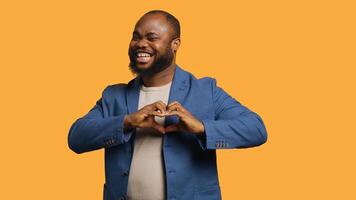 Portrait of jolly friendly african american man doing heart symbol shape gesture with hands. Cheerful nurturing BIPOC person showing love gesturing, isolated over studio background, camera A photo