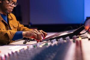 Audio engineer producing new tracks on console in control room, twisting knobs and pressing faders on soundboard panel. Music producer working on processing and editing music. Close up. photo