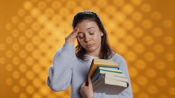 Woman with worried facial expression feeling migraine pain, carrying books for school exam, studio background. Stressed student with textbooks suffering headache from too much homework, camera B photo