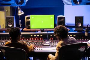 Team of audio experts mixing and mastering music next to mockup in control room, editing new tracks for an album. Sound designer working on mixing and mastering with console, software. photo