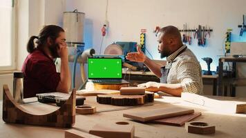 Woodworker looking over blueprints on green screen laptop in CAD software with apprentice. Craftsperson and coworker designing custom 3D furniture on chroma key notebook in studio, camera B photo