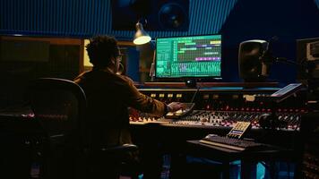 Tracking engineer working on a new album and recording hit song, handling mixing console with moving faders and colored meters. Skilled sound designer pushing sliders and levers. Camera B. photo