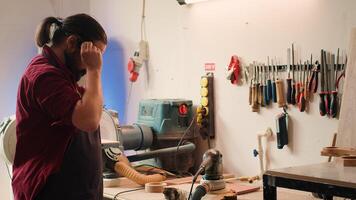 Artisan uses safety goggles to prevent workplace accidents while removing imperfections on wood. Man wearing protective equipment to avoid injury while using angle grinder to sander plank, camera A photo