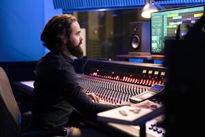 Audio engineer operating pc software for mixing and mastering tracks in studio, editing songs on control desk board. Music producer creating records with sliders and buttons, post production. photo