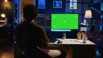 Self employed man doing IT support job from apartment personal office, coding on green screen PC. Software developer writing lines of code on mockup computer at home, camera B photo