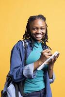 Portrait of happy girl smiling reading and writing for school exam on notepad, studio background. Jolly student grinning, completing papers for research needed for university classes photo