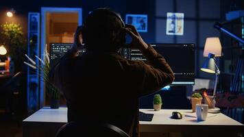 Technician putting headphones on while using coding to fortify firewalls, teleworking for IT company. Computer scientist listening music and upgrading binary code scripts in home office, camera B photo