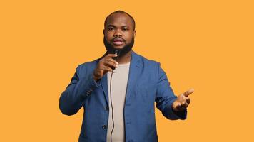 Portrait of african american lecturer holding monologue using microphone, gesturing with hands, studio background. Expressive BIPOC speaker talking during presentation using mic, camera A photo