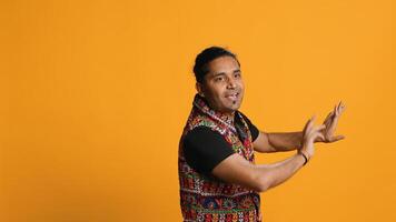 Joyful person having fun, dancing on rhythm, enjoying days off from work. Upbeat indian man entertaining himself doing funky movements, swinging arms, studio background, camera A photo