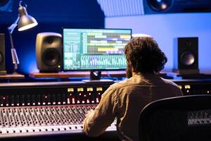 Audio technician processing and editing sounds in control room, operating on digital software app. Young sound expert mixing and mastering tracks in professional studio, mixer station. photo