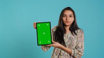 Person doing influencer marketing using isolated screen tablet, studio background. Indian woman holding empty copy space chroma key digital device, doing review, camera A photo