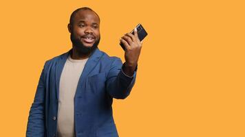 African american narcissistic man using cellphone to take selfies from all angles. Vain social media user taking photos using phone selfie camera, smiling happily, studio background, camera B