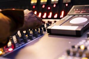 African american sound designer operates mixing console in control room, pushing sliders and buttons to adjust audio settings on records. Music engineer producing new tracks in studio. Close up. photo