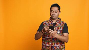 Indian man adding payment method on mobile phone website, purchasing stuff, isolated over studio background. Client does internet shopping, typing debit card info on cellphone, camera B photo