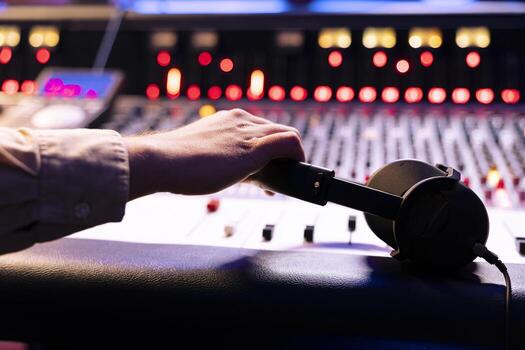 Audio expert grabbing headphones to check the final song in studio, editing music with sliders and buttons on control desk. Professional record producer composing new tracks. Close up. photo