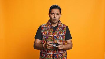 Cheerful man playing videogames with controller, studio background. Indian gamer smiling, having fun by participating in PvP online multiplayer game using console system, camera B photo
