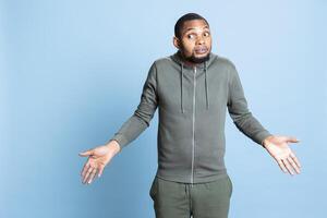 Clueless uncertain african american person acting confused and shrugging in studio, being doubtful and unsure about his answer. Young guy doing i dont know symbol in front of camera. photo