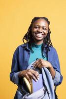 Portrait of happy BIPOC woman browsing through backpack, isolated over studio background. Joyous teenager taking out school textbooks out of rucksack used during commuting to university photo