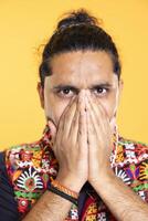 Portrait of troubled man covering mouth in disbelief, feeling saddened and rattled by events, isolated over studio backdrop. Close up shot of person on the verge of crying, left speechless by troubling news photo