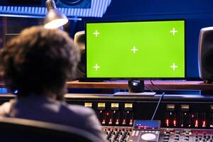 Music producer operates on control desk and mockup computer in professional studio, pressing key buttons and faders to create sounds. Young sound designer editing music and adding audio effects. photo