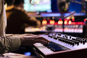 Male musician performing a hit song on electronic keyboard in recording studio, playing notes on midi controller to edit in post production. Artist singing in control room. Close up. photo