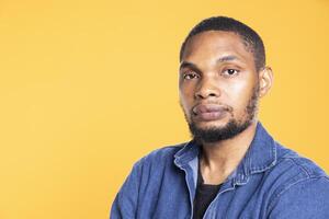 Portrait of african american serious man posing in front of the camera, standing with arms crossed against yellow background. Relaxed cool person feeling confident in studio. photo