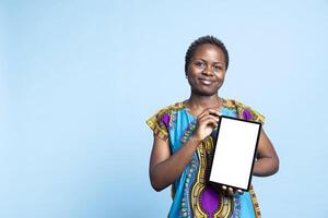 Confident woman showing tablet with blank mockup layout, creating advertisement with isolated copyspace template on wireless device. African american girl presents white display on camera. photo
