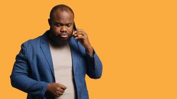 African american man having important phone call with business partner using smartphone, studio background. BIPOC person walking around discussing company matters during telephone call, camera A photo