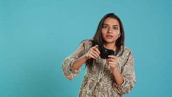 Jolly gamer celebrating after winning game on gaming console, studio background. Delighted Indian woman bragging after being victorious in videogame, defeating all enemies using gamepad, camera A photo
