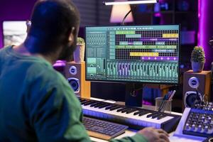 Audio engineer recording and producing new tunes on professional pc software, using mixing console and midi controller to create new music. Artist composer uses stereo gear at home studio. photo