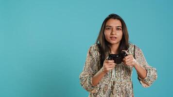 Cheerful indian gamer showing thumbs up sign gesturing while holding controller after winning videogame. Joyful woman enjoying games, doing approving hand gesture, studio background, camera A photo