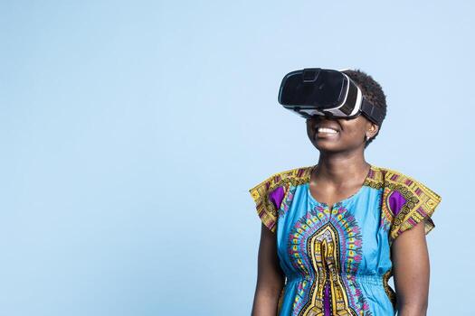 African american having fun with virtual reality glasses in studio, enjoying artificial intelligence with innovative 3d gadget. Modern person using vr headset with interactive vision software. photo