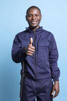 Happy confident security agent showing a thumbs up sign in studio, spreading positivity around and smiling. Cheerful african american guard doing a like symbol, approval gesture. photo