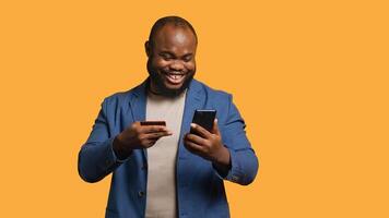 Happy man adding payment method on phone website, delighted to take advantage of promotions, studio background. Person thrilled to do internet shopping, typing credit card data on smartphone, camera A photo