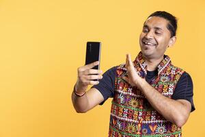 Happy man waving hand, chatting with friend over online videocall on smartphone, doing friendly gestures. Smiling person saluting mate on teleconference using mobile phone, studio background photo