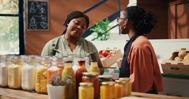 Vendor showing homemade sauces and dressings to buyer, promoting vegan nutrition and healthy lifestyle. Retailer presenting natural bulk items at local grocery store. Handheld shot. photo