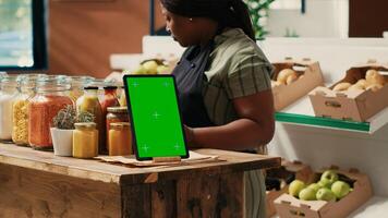 Device showing greenscreen template at local supermarket, tablet placed on store counter next to additives free sauces and pantry supplies in reusable jars. Merchant displaying copyspace screen. photo
