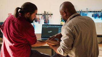 African american manufacturer and colleague comparing wood art piece with schematic displayed on CAD software on laptop. Woodworking professionals crosschecking wooden object with blueprint, camera A photo