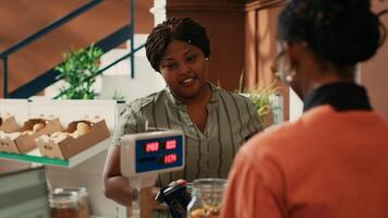 Local vendor counting and scanning goods for customer at bio natural supermarket, african american woman encourages nutritious food. Shopper on the lookout for non toxic produce at store. photo