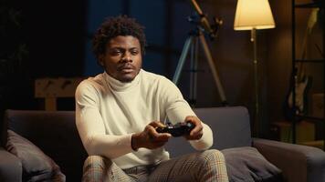 Focused BIPOC man plays intense online videogame, spamming attack buttons on controller. Gamer participating in internet esports competition, sitting on couch and playing on gaming console photo