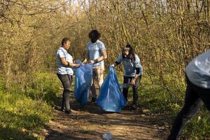 Team of environmentalists picking up rubbish from the woods, fight against pollution and protect the ecosystem. Volunteers doing community service to collect junk and plastic. photo