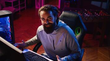 Content creator arriving in studio, sitting in gaming chair and talking with online viewers during livestream. Pro gamer streaming live from neon lit home, discussing with internet audience photo