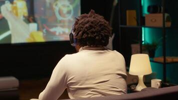 Man using headphones to discuss with teammates while playing videogame on ultrawide smart TV. Gamer chatting with online friends while enjoying game on gaming console in home theatre photo