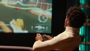 African american man playing shooter videogame on widescreen TV in futuristic setting with health, stamina, ammo bars HUD overlay. Close up shot of gamer enjoying PvP fps online multiplayer game photo